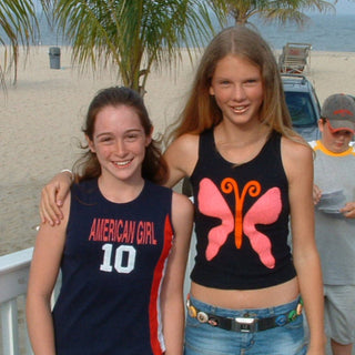 Two girls, Holly Armstrong and Taylor Swift, standing on a beach promenade in Point Pleasant, NJ with palm trees and ocean view.