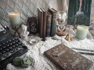 Vintage desk setup with typewriter, books, candles, and decorative items on a textured surface.